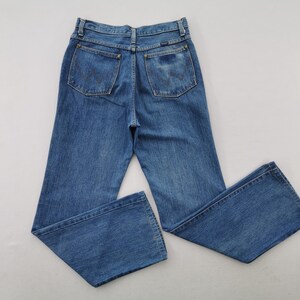 May include: Blue denim jeans with a classic five-pocket design. The jeans have a high waist and a straight leg. The back pockets feature a stitched design. The jeans are made of a medium-wash denim.