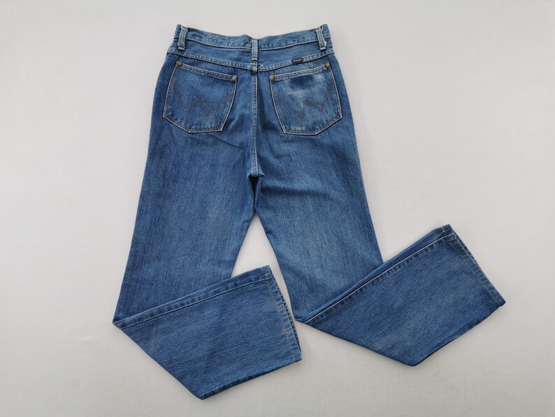May include: Blue denim jeans with a classic five-pocket design. The jeans have a high waist and a straight leg. The back pockets feature a stitched design. The jeans are made of a medium-wash denim.
