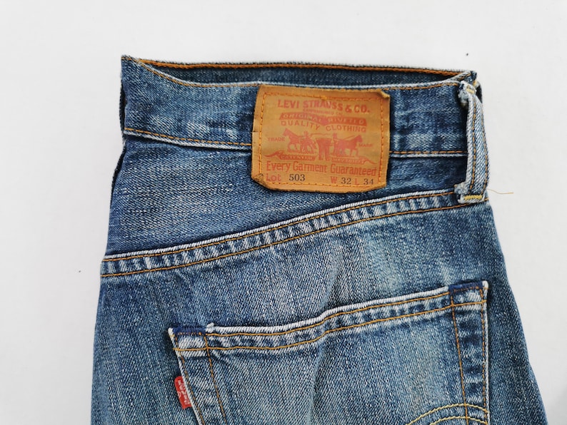 May include: Close-up of blue denim jeans with a brown leather patch. The patch features the Levi Strauss & Co. logo and text. The jeans have a classic five-pocket design and are labeled W 32 L 34.