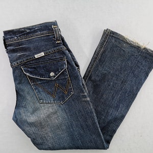 Puede incluir: Vaqueros de mezclilla azul oscuro con un efecto descolorido y un dise&ntilde;o cl&aacute;sico de cinco bolsillos. Incluye cierre de bot&oacute;n y cremallera, un peque&ntilde;o parche con el logotipo y un dise&ntilde;o distintivo de bolsillo trasero. Los vaqueros tienen una ligera abertura de pierna acampanada.