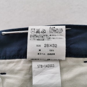 May include: Close-up of navy blue denim pants with a white interior. A tag displays the size 28x32, along with washing instructions and fabric composition. The tag also includes Japanese text and the number 578-142003.