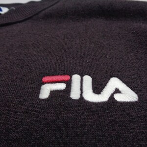 Pu&ograve; includere: Una felpa viola scuro con il logo del marchio FILA ricamato sul petto. Il logo &egrave; composto dalla parola FILA in filo bianco con una barra orizzontale rossa sopra la lettera I. Un'etichetta parziale del marchio &egrave; visibile sullo scollo.