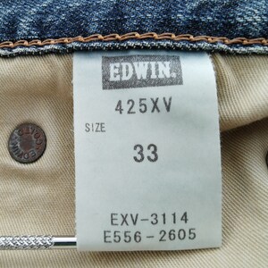 Puede incluir: Primer plano del interior de unos vaqueros azules. Una etiqueta blanca muestra "EDWIN", "425XV" y la talla "33". Se ven dos botones met&aacute;licos, uno con "EDWIN CO.". Los vaqueros son de estilo denim cl&aacute;sico.
