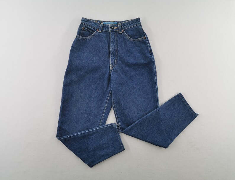 May include: Dark blue denim jeans with a high waist and straight leg. The jeans have classic five-pocket styling, a button and zipper closure, and belt loops. The denim is a medium weight, suitable for casual wear.