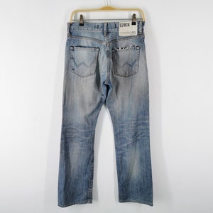 May include: Light blue denim jeans with a faded wash, hanging on a wooden hanger. The jeans have a classic five-pocket design, a straight leg, and the brand name "EDWIN" is visible on the back pocket.