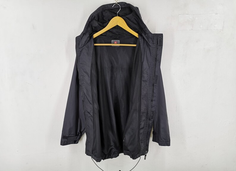 May include: Black hooded jacket with a mesh lining, hanging on a wooden hanger. The jacket has a zipper closure, a drawstring at the bottom, and a small logo on the chest. The jacket is displayed against a white background.