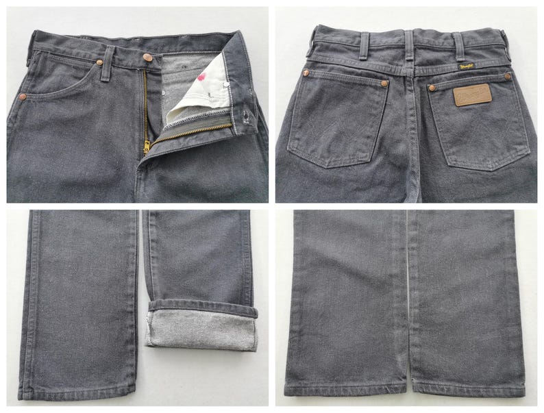 May include: Close-up shots of gray denim jeans. The jeans have a button and zipper closure, front and back pockets, and a leather patch. The bottom hem is cuffed, revealing the lighter fabric inside. The Wrangler brand is visible.
