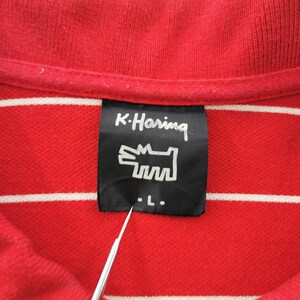 Puede incluir: Primer plano de un polo rojo con rayas horizontales blancas. La camisa presenta una etiqueta negra con el texto "K. Haring" y un gr&aacute;fico de perro estilizado. La etiqueta tambi&eacute;n indica una talla "L".