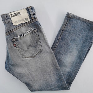 May include: Faded blue denim jeans with a distressed pocket and the brand name "EDWIN" on a tag. The jeans have a classic five-pocket design and a straight leg fit.