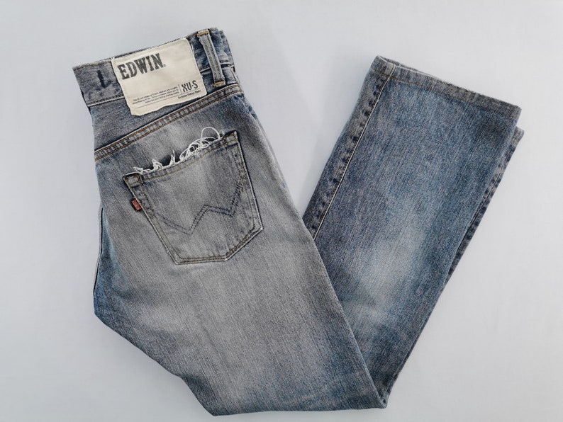 May include: Faded blue denim jeans with a distressed pocket and the brand name "EDWIN" on a tag. The jeans have a classic five-pocket design and a straight leg fit.