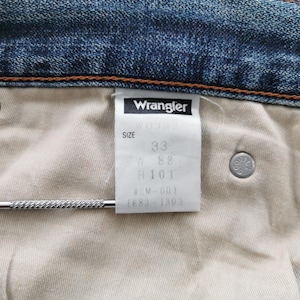K&ouml;nnte beinhalten: Nahaufnahme der Innenseite einer blauen Jeans mit einem wei&szlig;en Etikett mit der Aufschrift "Wrangler" und der Gr&ouml;&szlig;e 33. Die Jeans hat einen Knopf und einen Metallstab.