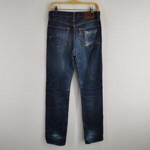 K&ouml;nnte beinhalten: Dunkelblaue Jeans mit Used-Look und klassischem F&uuml;nf-Taschen-Design. Die Jeans h&auml;ngen an einem Holzb&uuml;gel und zeigen die Ges&auml;&szlig;taschen und einen Leder-Markenaufn&auml;her.