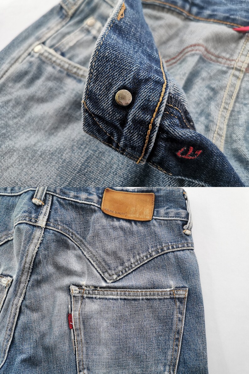 May include: Detailed shot of blue denim jeans, highlighting the button, pocket, and leather patch. The jeans have a faded look with visible stitching and a red tag. The leather patch reads "GENUINE QUALITY". The jeans are a classic style.