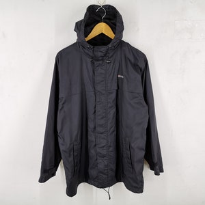 May include: A black hooded jacket with a drawstring at the waist and a small logo on the chest. The jacket is hanging on a wooden hanger against a white background. The jacket has a zipper closure and pockets.