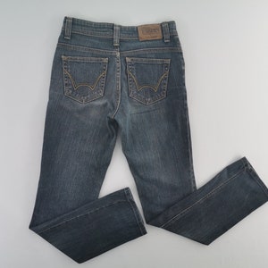 K&ouml;nnte beinhalten: Eine dunkelblaue Jeans aus Denim im klassischen F&uuml;nf-Taschen-Design mit einem braunen Lederaufn&auml;her am hinteren Bund mit der Aufschrift EDWIN und markanten goldfarbenen N&auml;hten auf den beiden Ges&auml;&szlig;taschen mit geschwungenem Bogenmuster.
