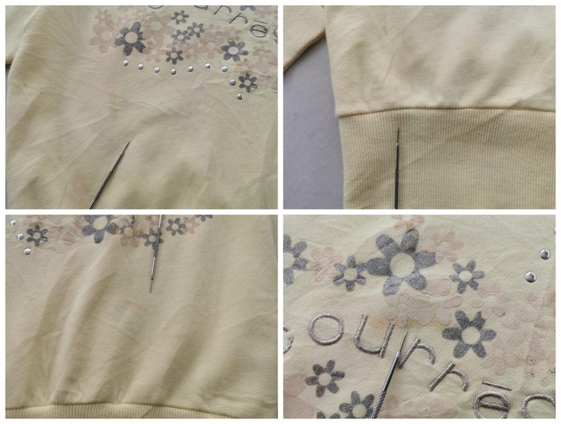 May include: A light yellow sweatshirt with a floral design and the word "ourre" embroidered on the front. The floral design includes gray and pink flowers with silver studs. The sweatshirt has a ribbed hem and cuffs.