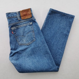 Puede incluir: Vaqueros de mezclilla azul medio con un diseño clásico de cinco bolsillos, un parche de cuero marrón claro en la cintura trasera con el texto Levi Strauss & Co y una pequeña etiqueta roja en el bolsillo trasero. Talla indicada 32 34.
