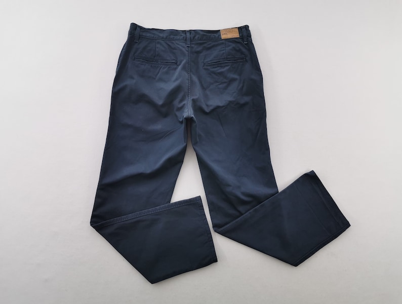 May include: Navy blue pants with a classic design. The pants feature a button and zipper closure, belt loops, and two back pockets. The pants are made of a soft, durable fabric.