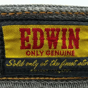 May include: Close-up of a denim label with the brand name "EDWIN" in red letters on a yellow background. The label also includes the text "ONLY GENUINE" and "Sold only at the finest stores."