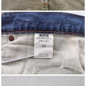 May include: Close-up of Wrangler denim jeans. The image shows the inside of the jeans with tags indicating size 33, model number WM0384, and care instructions. The Wrangler logo is visible.