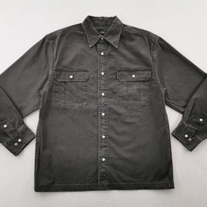 May include: A charcoal gray button-down shirt with two chest pockets and buttoned cuffs. The long-sleeved shirt has a classic collar and a row of white buttons down the front.