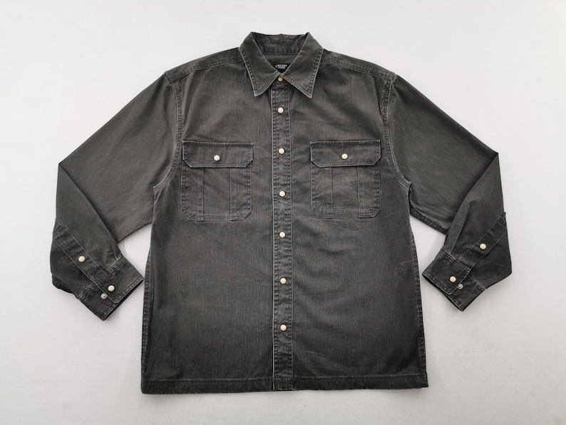 May include: A charcoal gray button-down shirt with two chest pockets and buttoned cuffs. The long-sleeved shirt has a classic collar and a row of white buttons down the front.