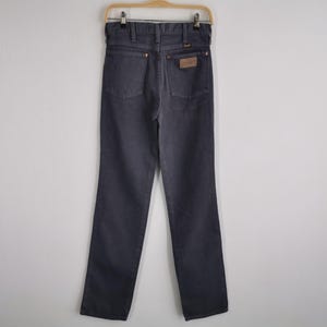 May include: Dark gray denim jeans hanging on a wooden hanger. The jeans have a classic five-pocket design, a brown leather patch on the back, and a straight leg cut. The jeans are made of a durable denim material.