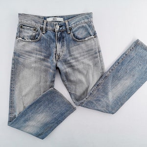 May include: Light blue denim jeans with a faded wash and a straight leg. The jeans have a button and zipper closure, front and back pockets, and a small label on the waistband. The jeans are laid flat on a white surface.