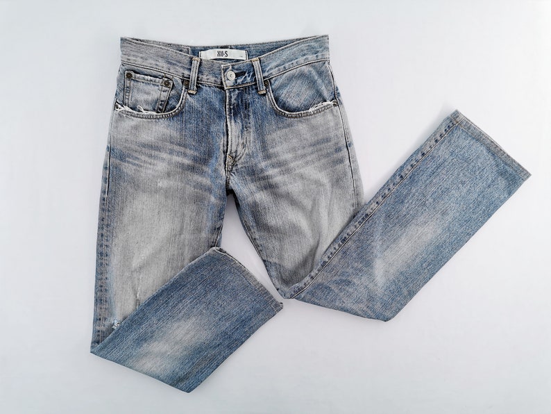 May include: Light blue denim jeans with a faded wash and a straight leg. The jeans have a button and zipper closure, front and back pockets, and a small label on the waistband. The jeans are laid flat on a white surface.
