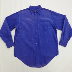 Puede incluir: Una camisa abotonada de manga larga en un tono azul vibrante. La camisa presenta un cuello clásico, un bolsillo en el pecho y puños abotonados. La tela tiene una textura de pana y los botones son de color latón.