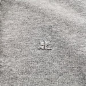 May include: Close-up of a gray, button-down garment. The fabric is a soft, textured knit. A small, embroidered logo is centered on the chest. Silver buttons are visible on the left side. The overall aesthetic is casual and comfortable.