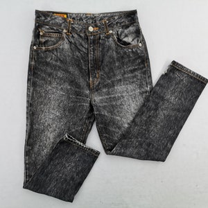 May include: Acid wash denim jeans with a classic five-pocket design. The jeans feature a button and zipper closure, belt loops, and a faded, textured appearance. The jeans are a dark gray color.