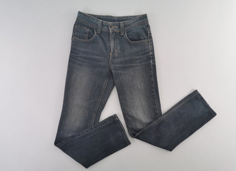 K&ouml;nnte beinhalten: Eine dunkelblaue Jeans aus Denim mit klassischem F&uuml;nf-Taschen-Design, Knopf- und Rei&szlig;verschluss sowie dezenten Abnutzungsspuren an den Oberschenkeln. Die Jeans hat einen geradlinigen Schnitt mit deutlich sichtbaren N&auml;hten an den Seiten.