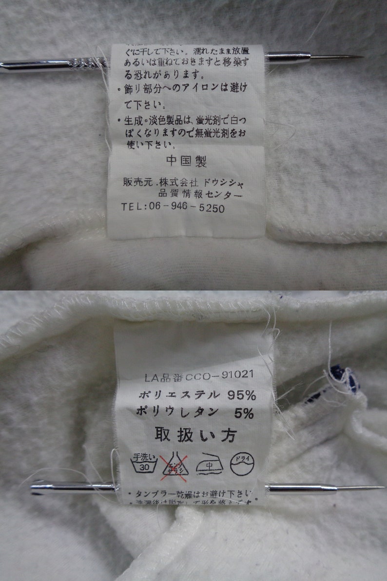 May include: Close-up of two white fabric tags with Japanese text and care symbols. The tags include information about the fabric composition: 95% polyester and 5% polyurethane. The tags are attached to a white fabric.
