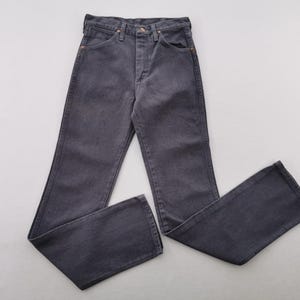 May include: A pair of dark gray denim jeans, laid flat. The jeans have a classic five-pocket design with a button and zipper closure. The fabric appears to be a medium weight denim.