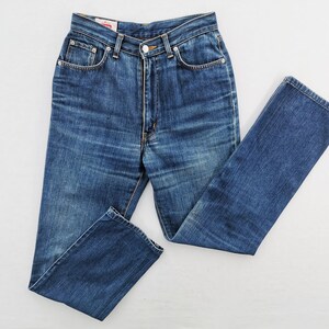 May include: Blue denim jeans with a classic five-pocket design. The jeans have a high waist and a straight leg. The fabric shows subtle fading and wear, typical of denim. The jeans are laid flat on a white surface.