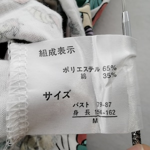May include: A white fabric tag with Japanese text indicating the composition of a garment: 65% polyester, 35% cotton. The tag also lists size information, including bust and height measurements, and the size M.
