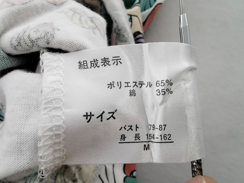 May include: A white fabric tag with Japanese text indicating the composition of a garment: 65% polyester, 35% cotton. The tag also lists size information, including bust and height measurements, and the size M.