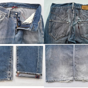 May include: Blue denim jeans with a classic five-pocket design. The jeans have a button and zip closure, with a distressed look and faded areas. The back features two pockets and a leather patch.