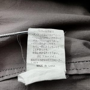 May include: Close-up of a gray fabric with a white tag attached. The tag has Japanese text and the words "MADE IN CHINA" printed in English. The fabric has a visible seam.
