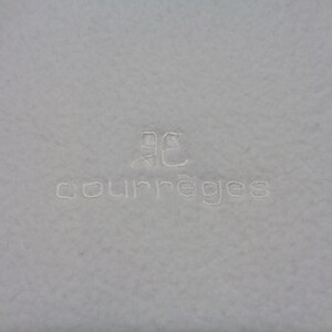 May include: A light gray textile with the embroidered word "courr&egrave;ges" in a matching light gray thread. Above the word is a stylized logo also embroidered in the same color.