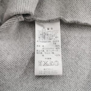 May include: Close-up of a gray sweatshirt with a pink trim. A white tag with Japanese text and care symbols is attached. The tag includes the material composition: 60% cotton, 40% polyester.