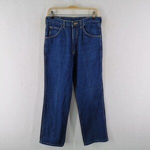 May include: A pair of classic blue denim jeans hanging on a wooden hanger. The jeans have a straight leg cut, five pockets, and a button and zipper closure. The denim is a medium wash, and the jeans appear to be new.