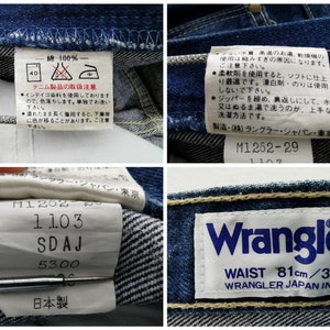 May include: Close-up of blue denim jeans with multiple tags. One tag reads "Wrangler" with "WAIST 81cm/32". Other tags include washing instructions and Japanese text. The jeans are made of 100% cotton.
