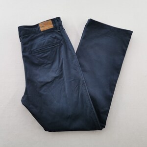 May include: Navy blue pants with a classic fit, featuring a button and zipper closure, belt loops, and back pockets. The pants have a subtle sheen and a relaxed silhouette, suitable for casual or semi-formal wear.
