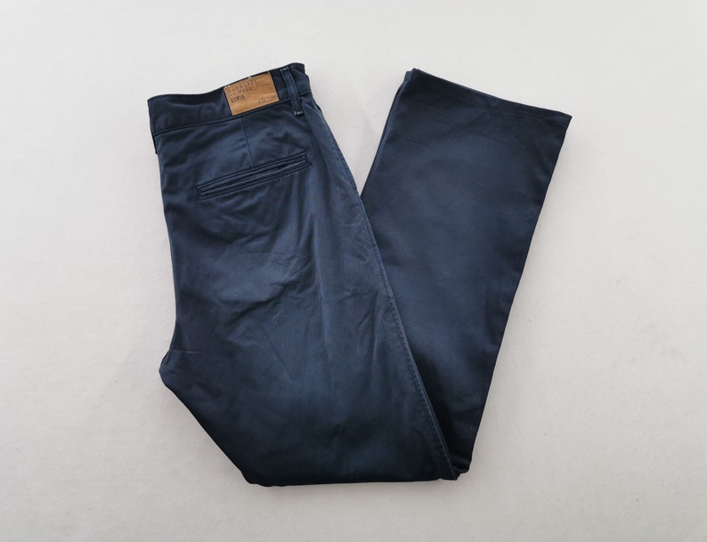 May include: Navy blue pants with a classic fit, featuring a button and zipper closure, belt loops, and back pockets. The pants have a subtle sheen and a relaxed silhouette, suitable for casual or semi-formal wear.