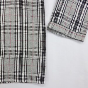May include: Close-up of a gray flannel shirt with a classic plaid pattern. The pattern features black, white, and thin red lines. The sleeve cuff is visible, showing the same plaid design. The shirt is buttoned and appears to be made of a soft fabric.