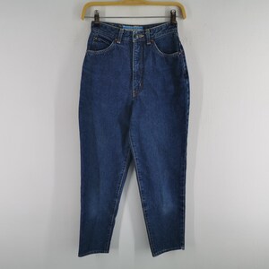 May include: Dark blue denim jeans hanging on a wooden hanger. The jeans have a high waist, pockets, and a button and zipper closure. The denim appears to be a medium weight, with a classic, straight-leg fit.