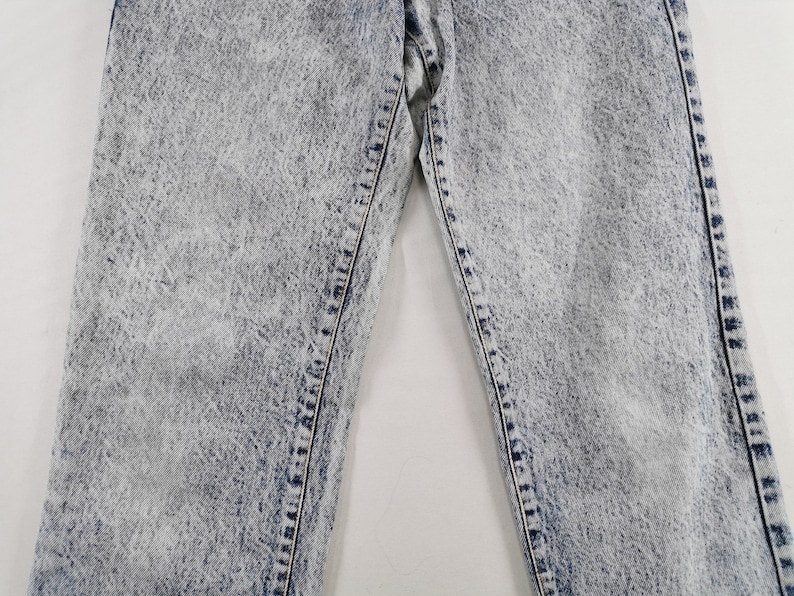 K&ouml;nnte beinhalten: Nahaufnahme einer Jeans aus Acid-Wash-Denim. Die Jeans hat ein hellblaues und wei&szlig;es, gesprenkeltes Muster mit sichtbaren N&auml;hten und Steppn&auml;hten. Das Bild konzentriert sich auf den oberen Teil der Jeans und zeigt die Textur und den Stil.