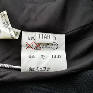 May include: Close-up of a garment's interior, showcasing care instructions and fabric composition. The label reads "ECO 11AR 0" with symbols indicating washing and drying guidelines. The fabric is 100% wool.